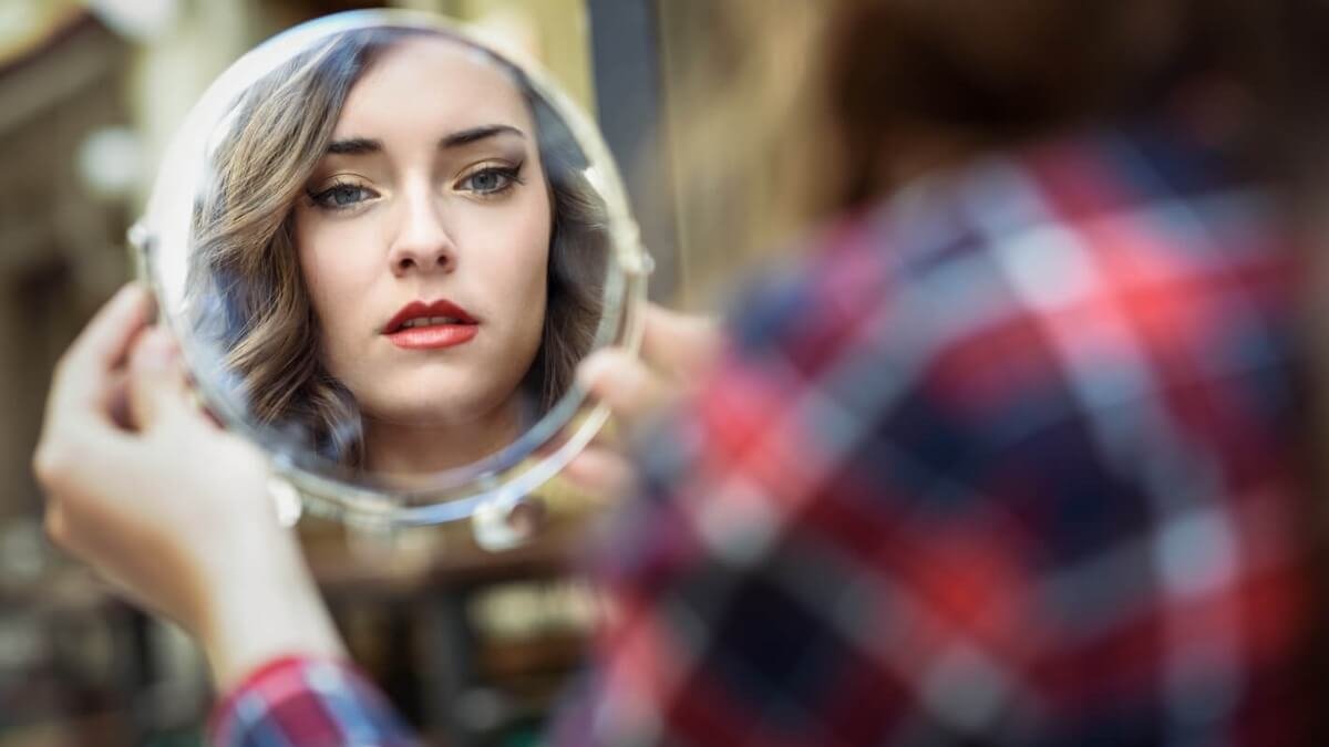 Mujer observándose al espejo con una mirada de autoexploración y aceptación consciente.
